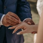 a groom putting on the wedding ring on bride s finger